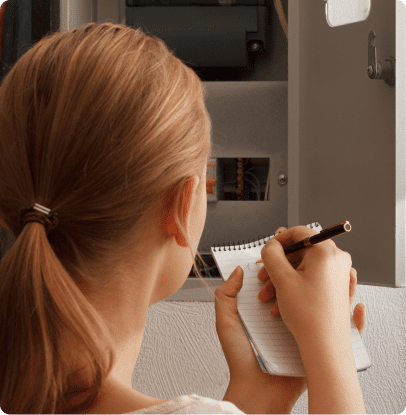 Person writing in notebook by electrical box